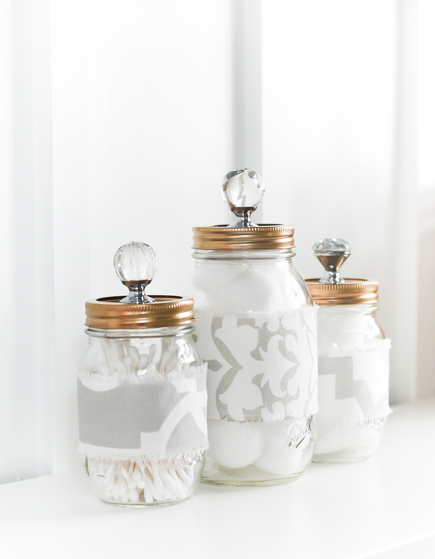 Pretty Bathroom Storage Mason Jars - Fabric Covered Mason Jars with Gold Spray Painted Lids and Crystal Knobs.