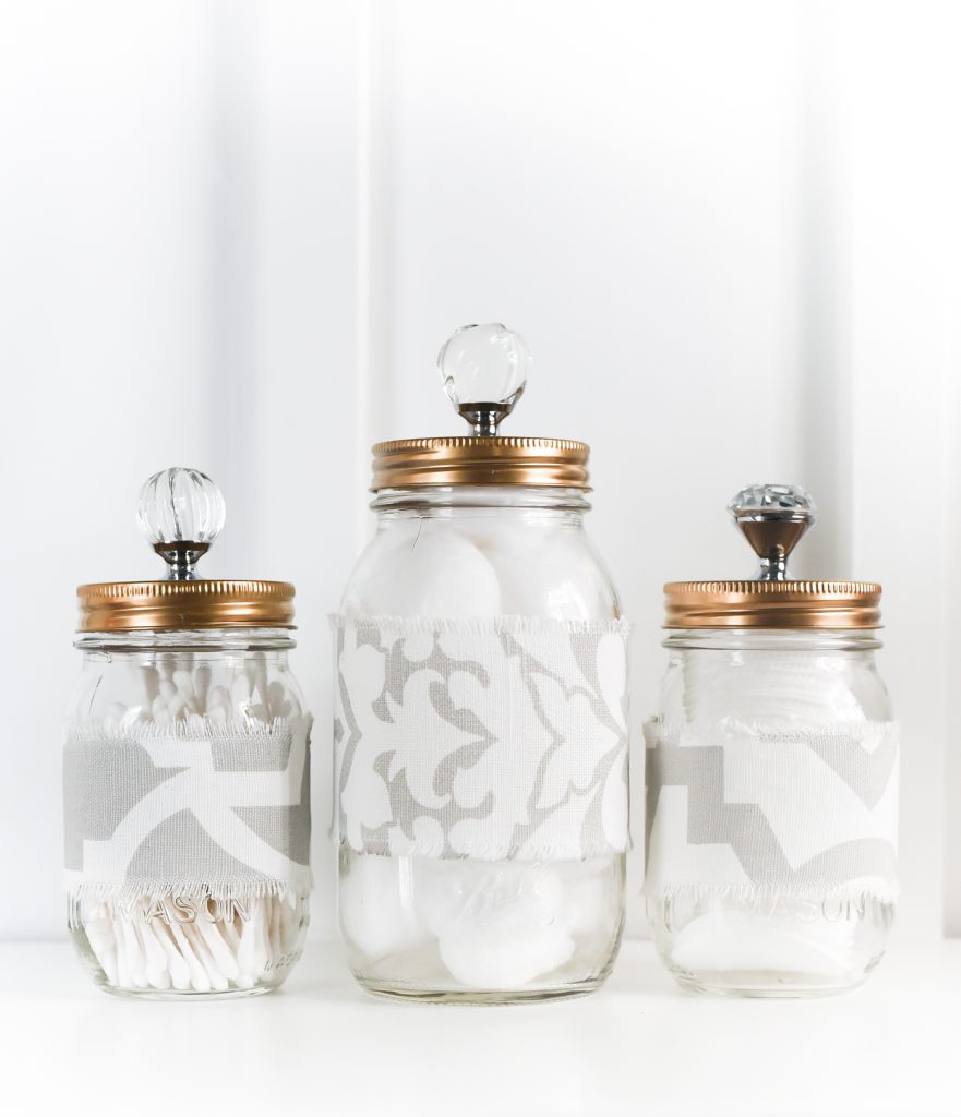 Mason jar bathroom storage jars with fabric cozies and gold tops with crytal knobs. Mason Jar Bathroom Storage and Organization Ideas. Organizing the bathroom with mason jars. Pretty storage ideas with mason jars. Rustic storage ideas with mason jars. Bathroom storage using mason jars.