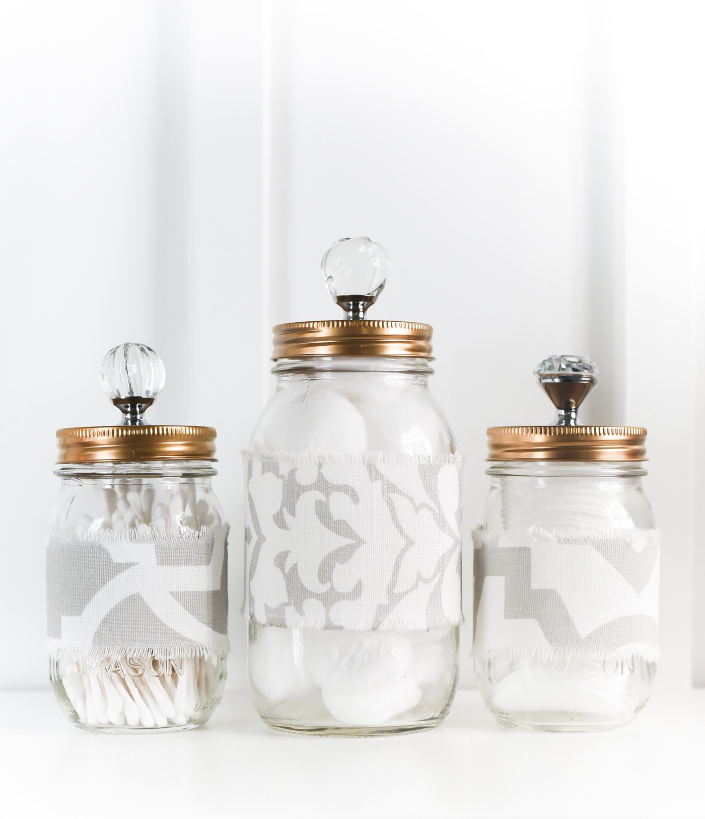Mason jars with knobs attached to tops. Gold spray painted mason jar lids with knobs. Fabric covered mason jars. Fabric mason jar cozies. Gray and white mason jars with gold spray painted lids.