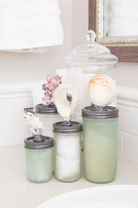 Seashell Topped Mason Jar Bathroom Storage. Mason Jar Bathroom Storage and Organization Ideas. Organizing the bathroom with mason jars. Pretty storage ideas with mason jars. Rustic storage ideas with mason jars. Bathroom storage using mason jars.